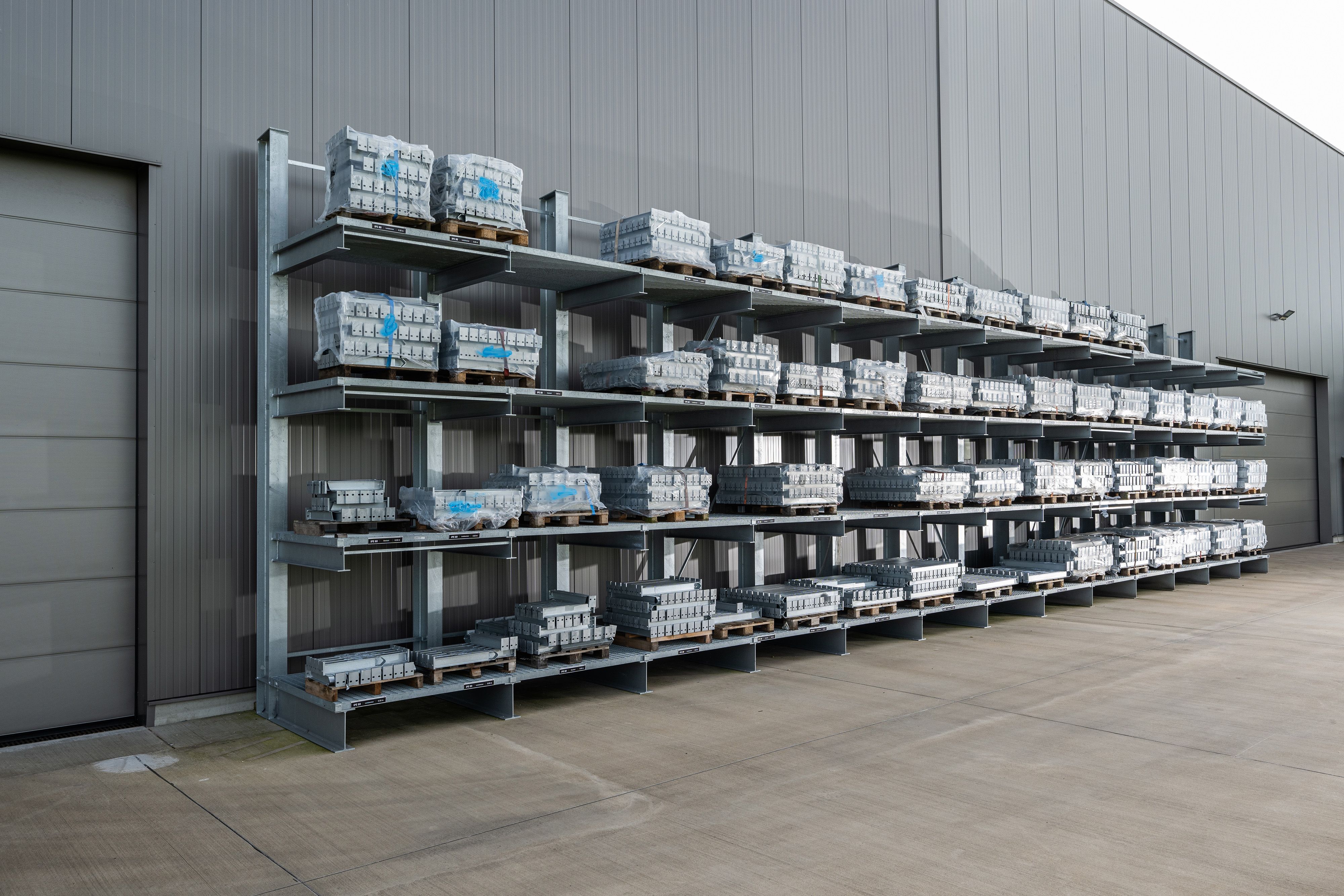 Metallregal mit mehreren Paletten gestapelt vor einer großen grauen Lagerhallenwand auf Betonboden